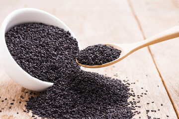 Poppy seeds in a white cup and in a wooden spoon placed on an old wooden table
