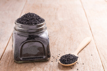 Poppy seeds in a glass jar and in a wooden spoon placed on an old wooden table