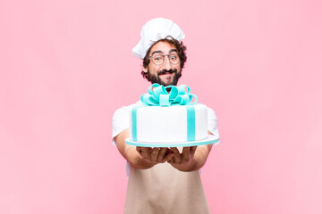 young crazy baker man holding a cake against pink wall