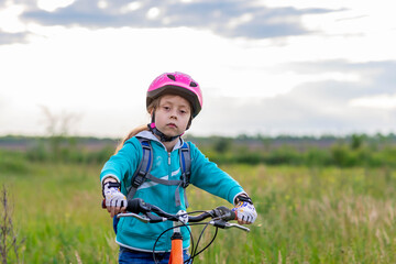 Fototapeta na wymiar A child in a bicycle helmet stands with a bicycle in the meadow.