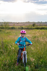 Fototapeta na wymiar A little girl in a bicycle helmet stands with a bicycle in the meadow.