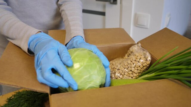 Volunteer in gloves with food donation box puts vegetables to help others. donation box with foodstuffs. Video footage Full HD