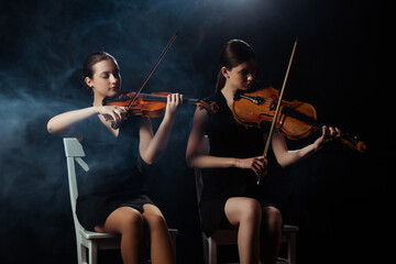 attractive musicians playing on violins on dark stage with smoke © LIGHTFIELD STUDIOS