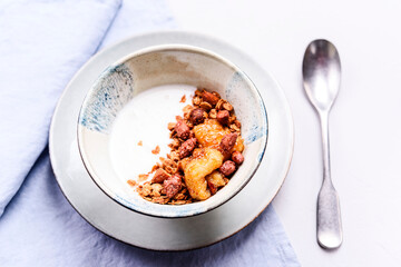 Healthy breakfast yogurt bowl with granola and caramelized bananas and nuts on grey concrete background. Selective focus