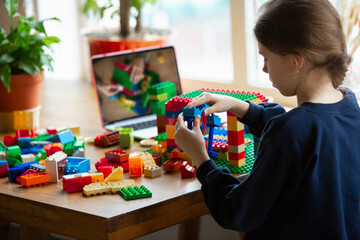 Girl playing with constructor at home, watching teacher's online tutorial on laptop. Digitalization, remote education concept. Technologies and devices. Man showing, giving online lesson. Artwork.