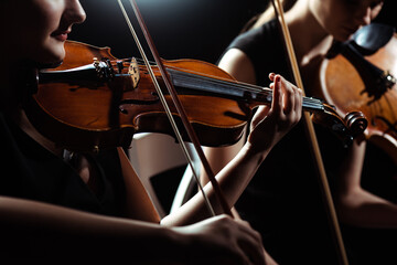 cropped view of two female professional musicians playing on violins on dark stage - obrazy, fototapety, plakaty