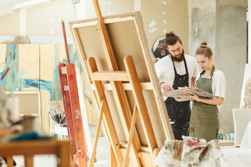 Wide angle portrait of creative couple painting picture together while standing by easel in art...