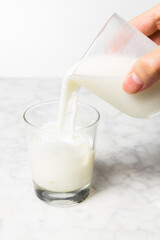 Man's hand pouring fresh milk into a glass with ice cubes. Dalgona coffee preparation