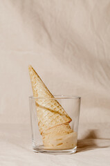 Ice cream waffle cone in glass on beige pastel background. Summer minimalism monochrome creative concept