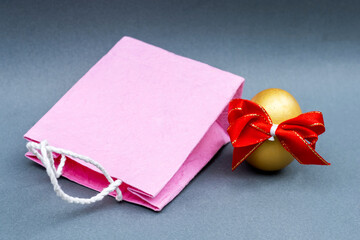 Golden Egg with red Ribbon and pink shopping bag isolated on gray background