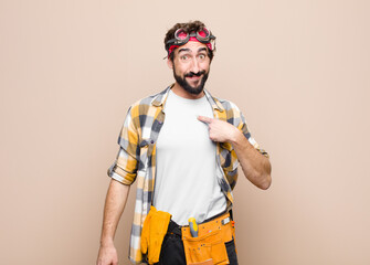 young housekeeper man looking happy, proud and surprised, cheerfully pointing to self, feeling...