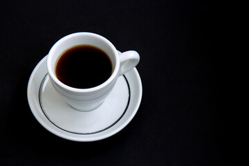 Fototapeta na wymiar Black coffee in a white cup on a saucer isolated on a black background. Selective focus. Side view