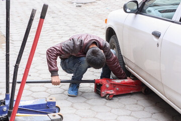 A man replaces the wheels on a car with tire fitting jack