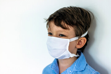 Portrait close up of little boy child in blue shirt wearing white protective mask during pandemic.Side view photo of boy looking away,wearing a protective mask while seeking protection from COVID-19.