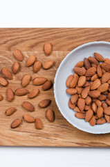 Flatlay view of almond seeds in light bowl on wooden table