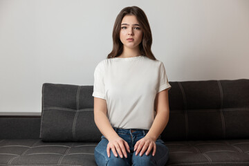 young beautiful brunette woman sitting on the sofa in her appartment holding hands on her legs looking calm, feels cozy at home