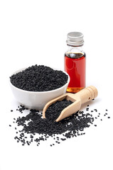 Black cumin seeds in bowl and essential oil in glass bottle. Nigella sativa isolated on white background.