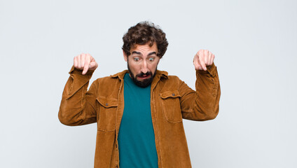 young handsome man feeling shocked, open-mouthed and amazed, looking and pointing downwards in...