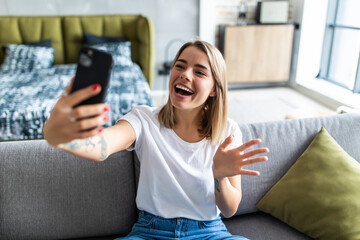 Photo of charming lady holding telephone making selfies speaking skype waving palm saying hi...