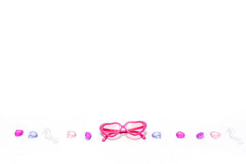 Children's pink heart-shaped glasses on a white background with glass decorations on a marine theme. Layout with space for text. Ready to travel and beach holidays at sea, sun protection, children's f