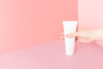 Young female hands holding blank white squeeze bottle plastic tube on pink background. Packaging of cream, lotion, gel, facial foam or skincare. Cosmetic beauty product branding mock-up. Copy space.