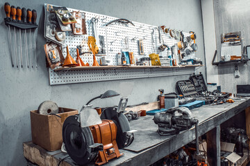 Garage. Workspace moto auto workshop closeup. Workbench with vise, grinder, sets of keys, tools kit,  equipment, spare parts. Old tools hanging on steel wall in the workshop as background, Tool shelf