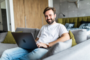 Handsome young man working on his laptop while relaxing on the sofa at home