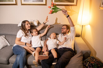 Bella famiglia si diverte nel salotto di casa mentre il papà cerca di dare dei fiori alla mamma