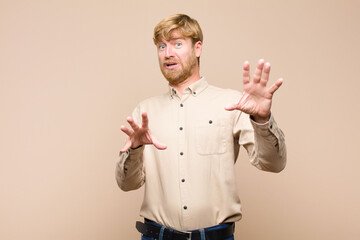 young blonde man feeling terrified, backing off and screaming in horror and panic, reacting to a...