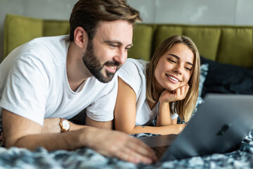 Happy young couple using laptop on bed at bedroom
