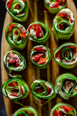 Fototapeta na wymiar Cucumber rolls with tomato and cream cheese close up on a wooden plate. Cucumber rolls with cheese. Delicious foot plate. Green rolls with salmon, cream cheese and red sweet peppers. Close up.