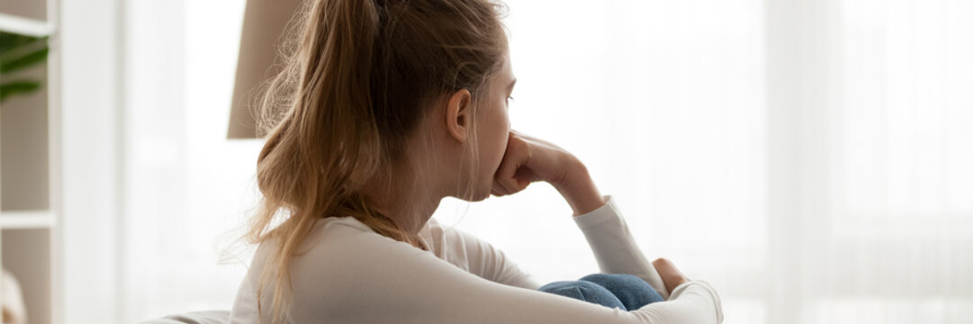 Girl sit on couch looking in distance out the window feels frustrated. Break up with boyfriend, personal life problems, unwilling pregnancy concept. Horizontal photo banner for website header design