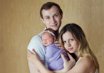 A woman and a man hold a newborn in their arms. Mom, dad and baby. Portrait of a young smiling family with a newborn in their arms. Happy family.