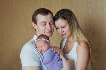 A woman and a man hold a newborn in their arms. Mom, dad and baby. Portrait of a young smiling family with a newborn in their arms. Happy family.