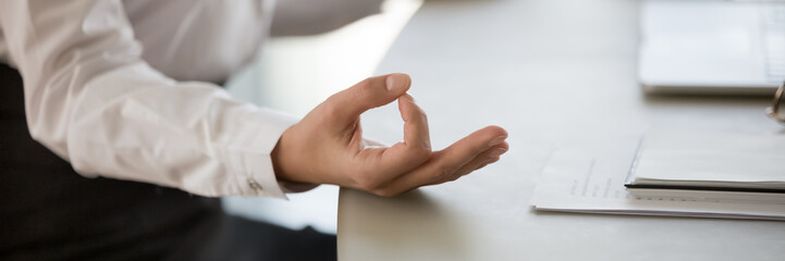 Calm business woman sitting at desk doing meditation practice close up view on folded fingers mudra...