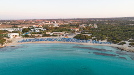 Aerial bird's eye view of Landa beach, Ayia Napa, Famagusta, Cyprus. Landmark tourist attraction golden sand bay at sunrise with sunbeds, sea restaurants at Makronissos and nissi, Agia Napa from above