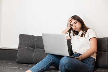 young beautiful woman working from home in her laptop sitting on the sofa in her appartment during quarantine isolation looks exhausted, stay safe home concept