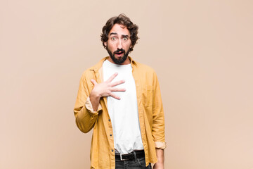 young crazy cool man feeling shocked, astonished and surprised, with hand on chest and open mouth,...