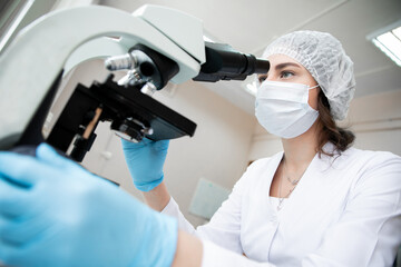 girl laboratory assistant in blue gloves and a cap looks through a microscope in a laboratory