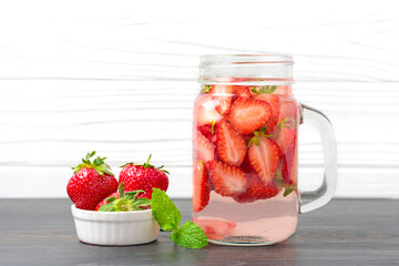 Strawberry infused water, cocktail, lemonade or tea. Summer iced cold drink with strawberry, leaf of mint, ice cube on white wooden background Flat lay