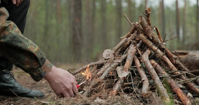 Man starts a fire in the forest using a lighter.  Close-up of a man's hand lighting a fire with a lighter. Lighting a fire in the forest by a person. Low angle of a burning fire made of brushwood.