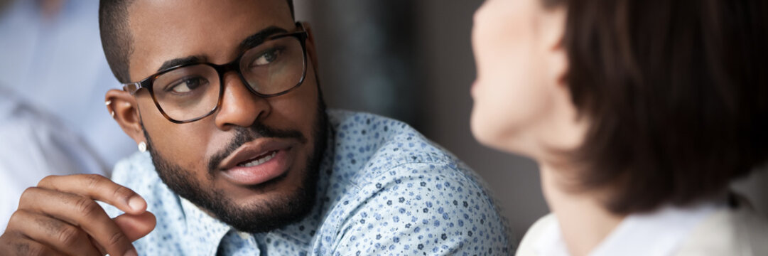 Multiethnic colleagues work together on common project share ideas considering solving communicating during meeting in office focus on American man. Horizontal photo banner for website header design