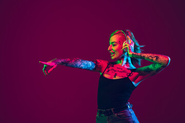 Listening to music, dancing with wireless headphones. Portrait of young caucasian woman on purple background in neon light. Human emotions, facial expression, sales, ad concept. Freak's culture.