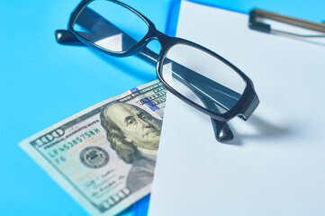 Blank clipboard with banknote of 100 dollars near glasses. Marketing concept