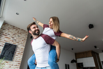 Portrait of funny comic couple, strong man carrying on back cheerful woman in piggy back gesturing...