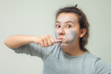 A teenage girl with a cosmetic mask on her face brushes her teeth. Facial scrub mask. The concept of health and beauty.