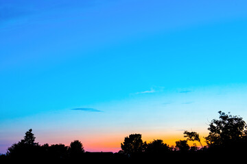 Fototapeta na wymiar An orange sunset against a blue sky in the shade of trees