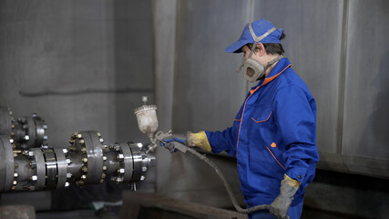 Worker in protective respirator paints oil and gas wellhead tree equipment with spray gun in production plant. Equipment for wellhead conncetion of oil and gas wells.