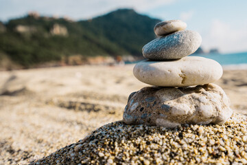 Fototapeta na wymiar Stones pyramid on pebble beach symbolizing stability, zen, harmony, balance with mountain and sky in background.