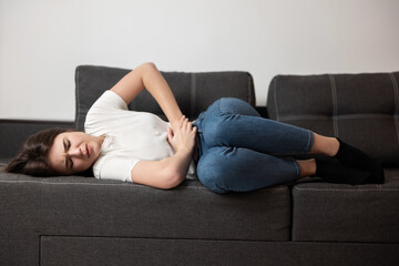 young beautiful brunette woman lying on the sofa suffering from extreme pain in stomach during periods looking desperate, healthcare and medical concept